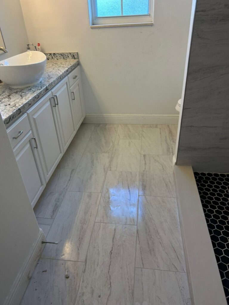 Bathroom with white cabinets, marble countertop, tiled floor, and a partially visible walk-in shower with black hex tile.