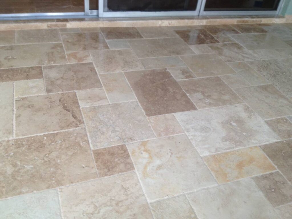 Beige and light brown stone tiles arranged in a rectangular pattern on a floor near a glass door.
